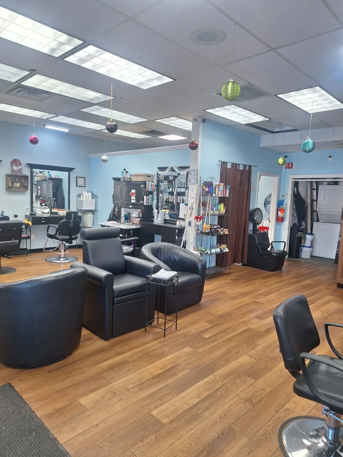 Inside the shop: black styling chairs and a shampoo station on a wood floor, with light blue walls and a shelf of hair products
