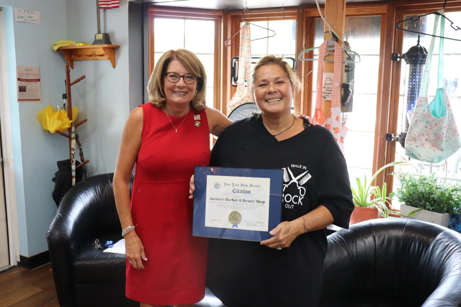 Aurora with a New York State senator in the shop, holding the framed Senate citation for Aurora’s Barber & Beauty Shop’s ten years
