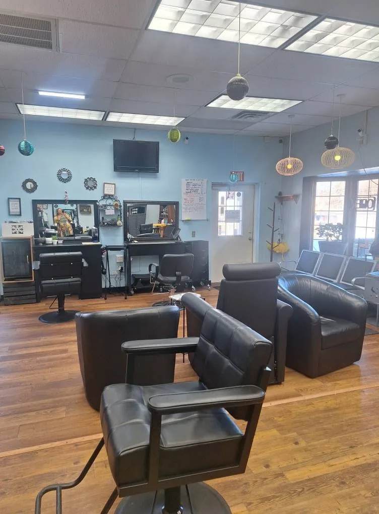 Two styling stations with mirrors along a light blue wall, and black leather chairs in front