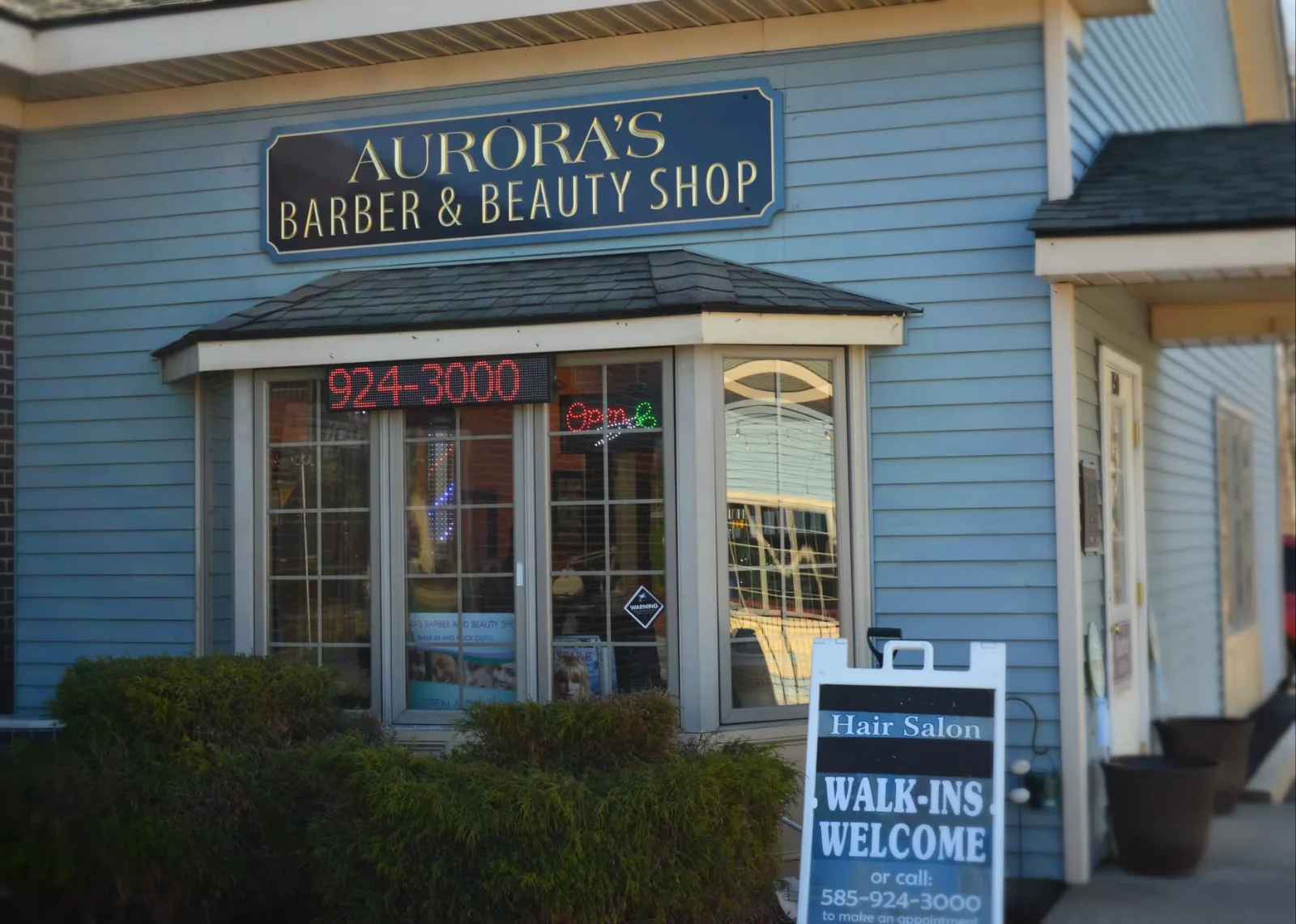 The shop front: a navy sign with gold letters reading Aurora’s Barber & Beauty Shop over a bay window, and a Walk-ins Welcome board outside