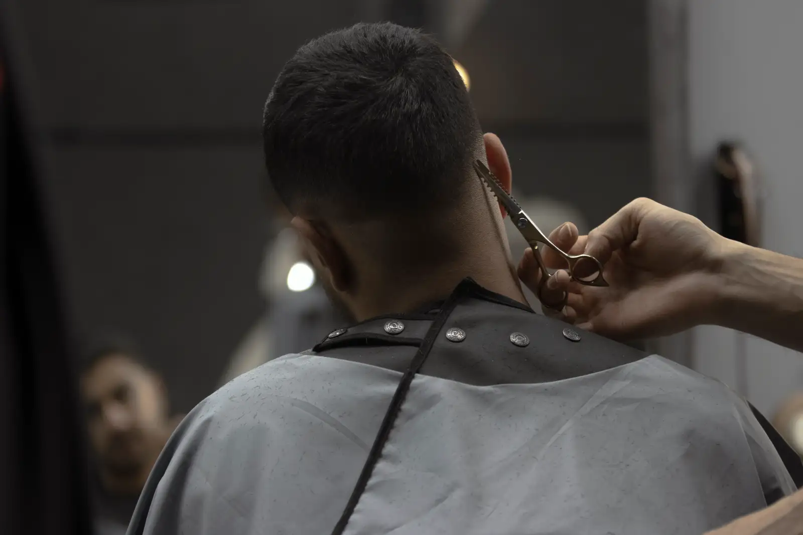 A barber’s hands trimming the back of a client’s head with scissors and a comb